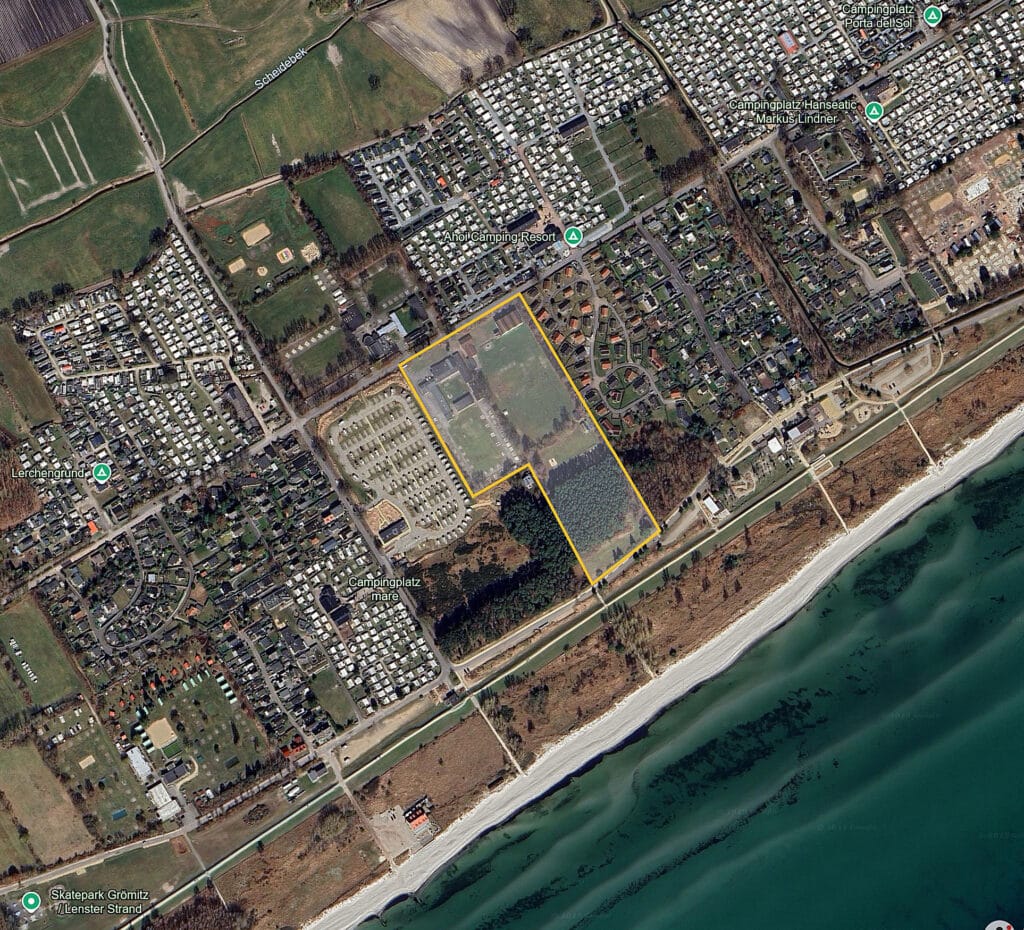 Bei dem Bild handelt es sich um eine hochauflösende Luftaufnahme, die ein weitläufiges Gebiet entlang der Küste einfängt und einen Überblick über eine vorstädtische und halbländliche Umgebung bietet, die mit Elementen der Natur verflochten ist. Beginnend in der unteren linken Ecke sehen wir den Rand eines Sandstrandes, der auf ruhiges, blaues Wasser trifft, was auf die Nähe zum Meer hindeutet. In der Höhe beginnt der Übergang von der natürlichen Strandumgebung zu den bebauten städtischen Gebieten. Es gibt einen Flickenteppich aus verschiedenen Landnutzungen – eine Mischung aus grünen Freiflächen, die zwischen Gebäudegruppen durchsetzt sind, die wie Wohnhäuser aussehen. Der Grundriss der Bebauung deutet auf eine geplante Gemeinschaft mit unterschiedlichen Straßen und Grundstücken hin. In der Mitte des Fotos befindet sich eine große Fläche, die mit einem gelben Rechteck hervorgehoben ist und ein Grundstück markiert, das aufgrund seiner Isolierung von den umliegenden bebauten Gebieten hervorsticht. Um dieses markierte Gebiet herum befindet sich etwas, das wie ein dichter Wald aussieht, was darauf hindeutet, dass es trotz der städtischen Umgebung immer noch natürliche Grünflächen in Reichweite gibt. Rechts und etwas oberhalb des zentralen Bereichs befinden sich Beschriftungen mit Standorten wie "Ahol Camping Resort", "Skatepark Grömitz / Lenster Strand" und "Campingplatz Ponta del Sol". Diese Bezeichnungen weisen auf bestimmte Freizeiteinrichtungen in der Umgebung hin. Darüber hinaus gibt es im oberen linken Teil des Bildes eine weitere Beschriftung, die auf den "Lerchengrund" hinweist. Auf dem gesamten Bild kann man sehen, dass sich verschiedene Straßen kreuzen, die verschiedene Teile der Gemeinde verbinden und Zugang zu allen aufgeführten Einrichtungen bieten.
